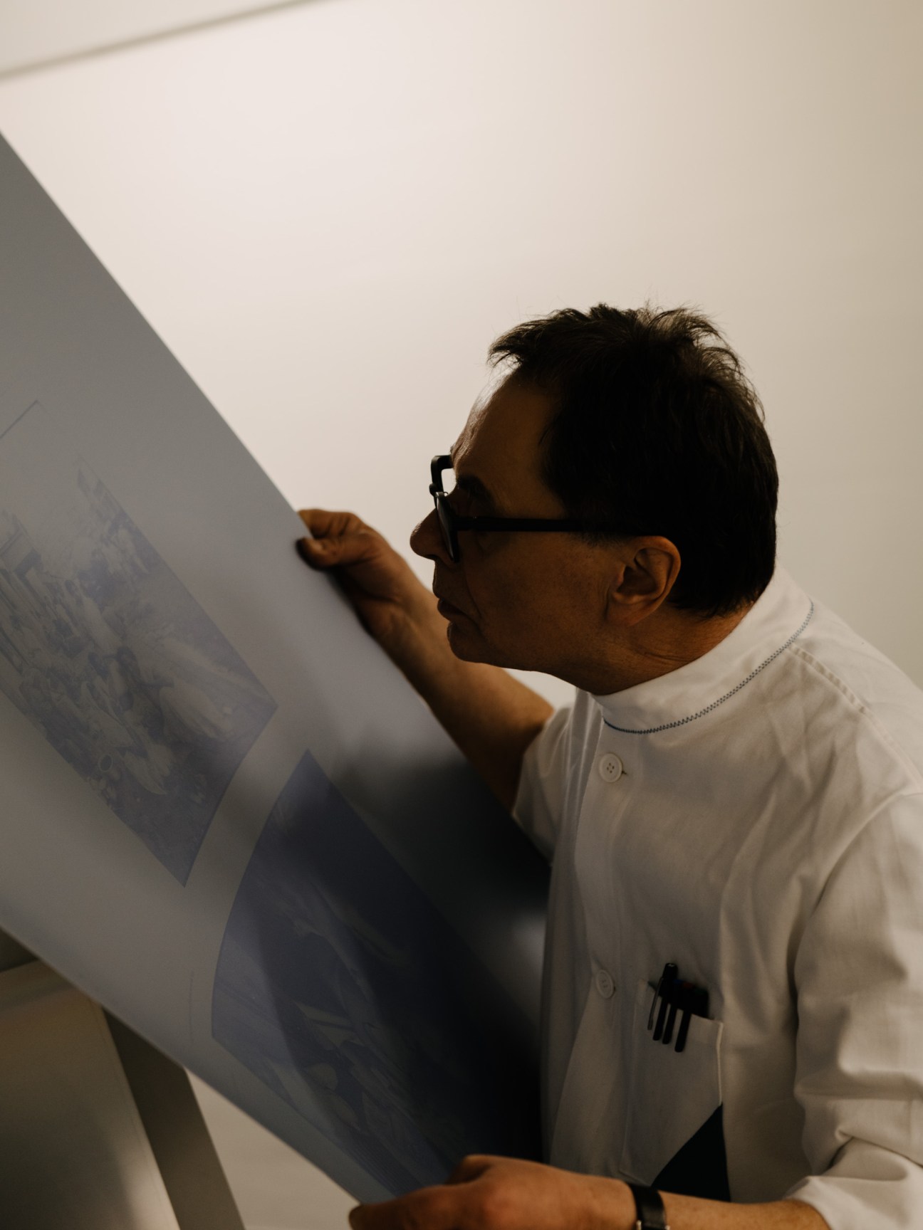 Gerhard Steidl examines a printing plate through his glasses while wearing a white shirt.