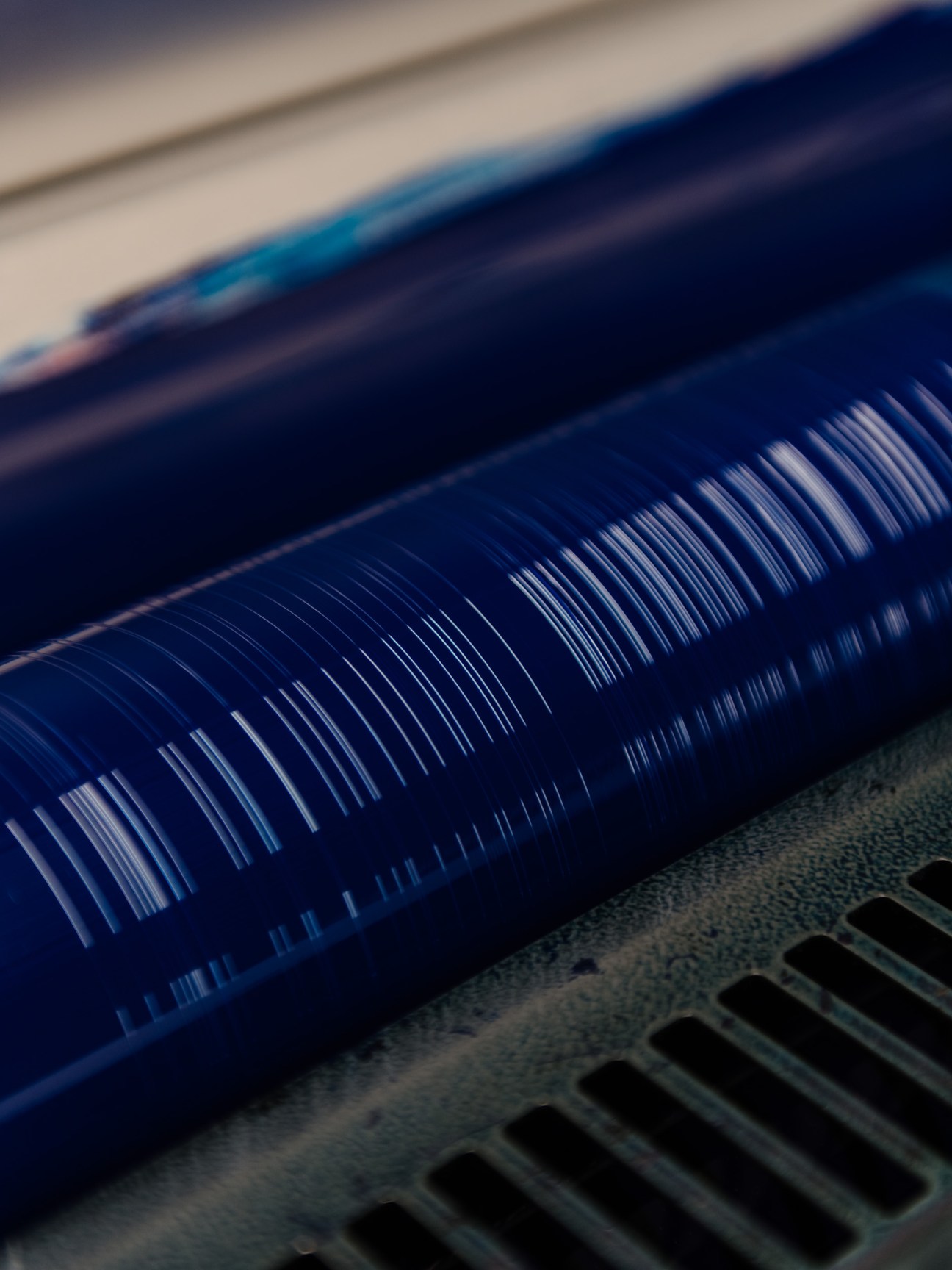 Close-up of blue ink being applied to a printing plate with a roller on offset printing equipment.
