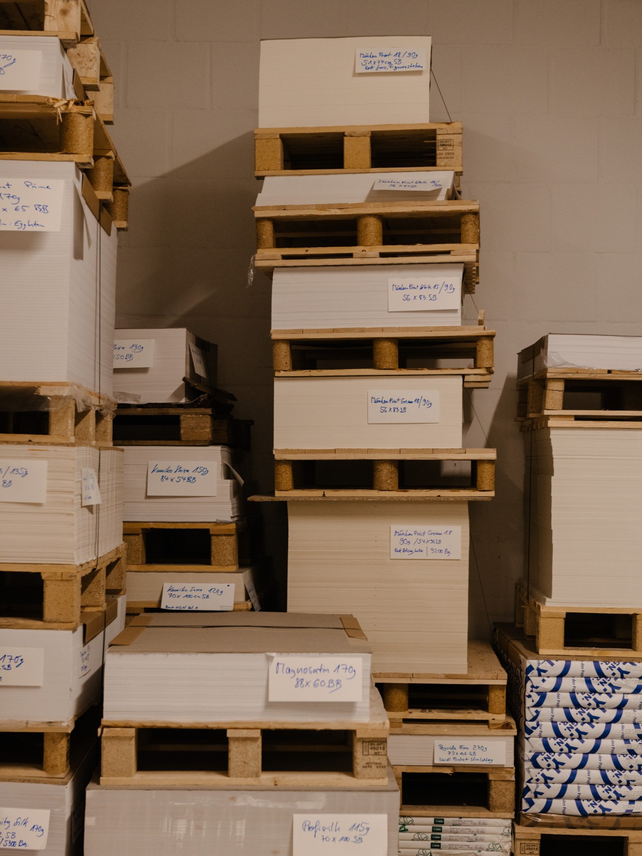 Stacks of paper stored on wooden pallets with handwritten labels in Steidl's warehouse.