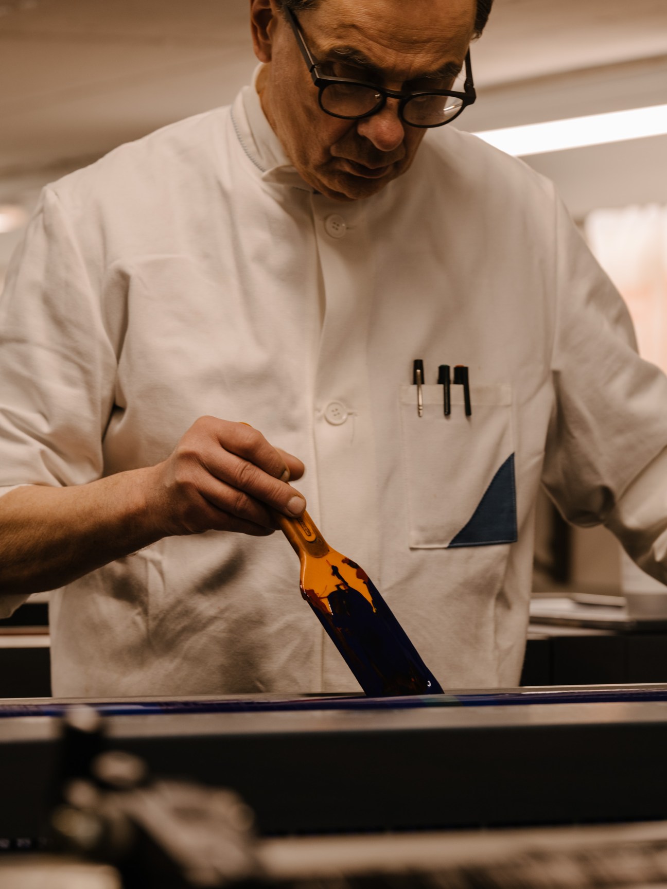 Gerhard Steidl in white shirt and glasses checks ink viscosity with a tool during printing production.