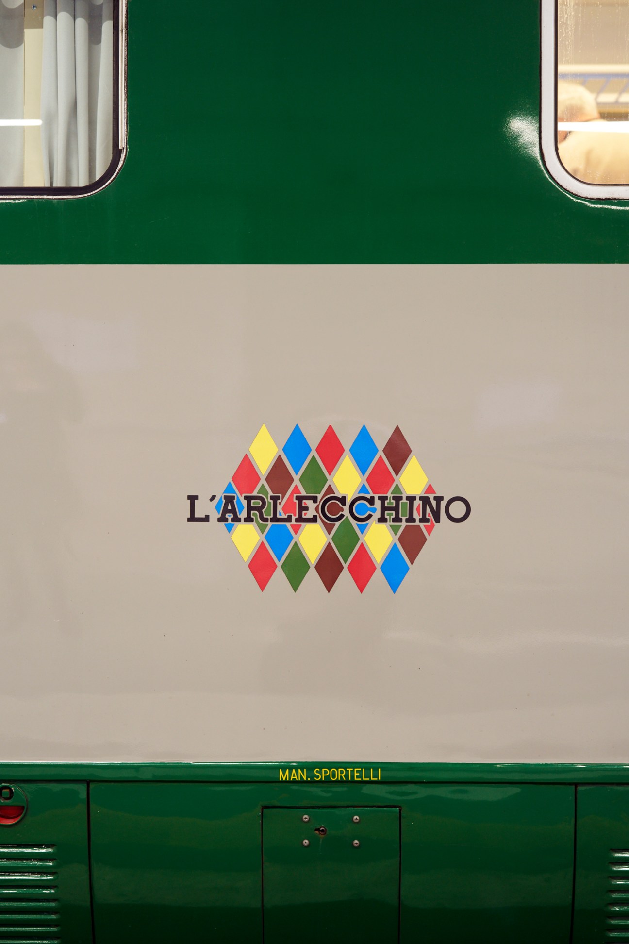 Side view of L'Arlecchino train showing colorful diamond-pattern logo on cream and green exterior