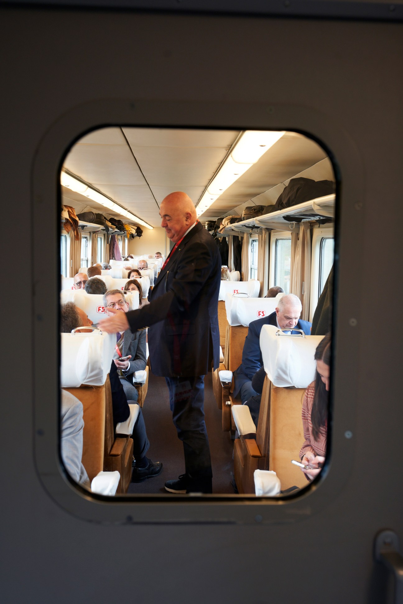 Interior of L'Arlecchino train showing passengers seated in first-class seats with white headrest covers