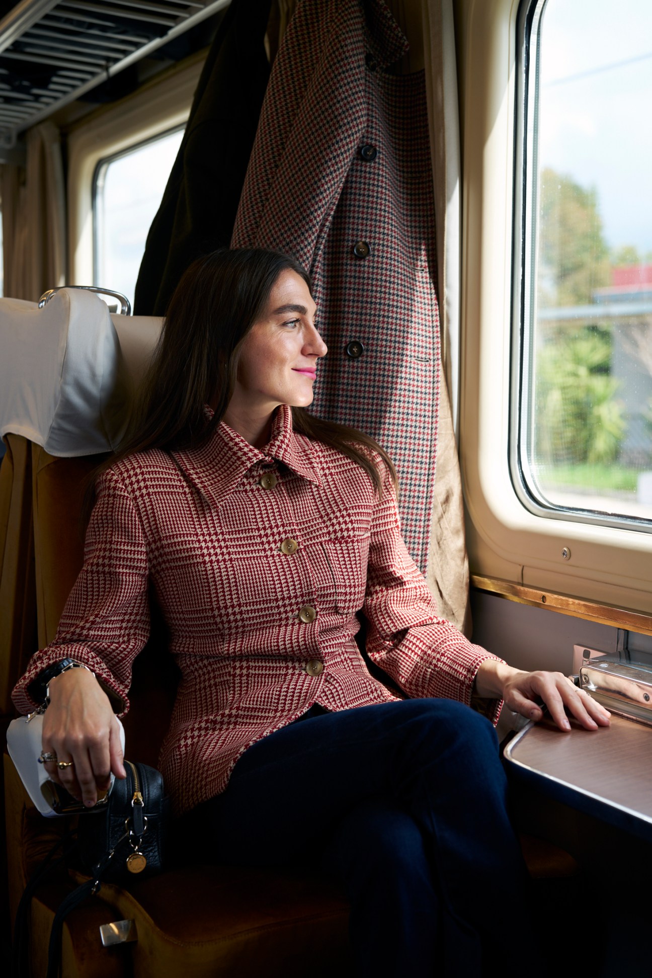Woman in checkered blazer sitting by train window looking outside
