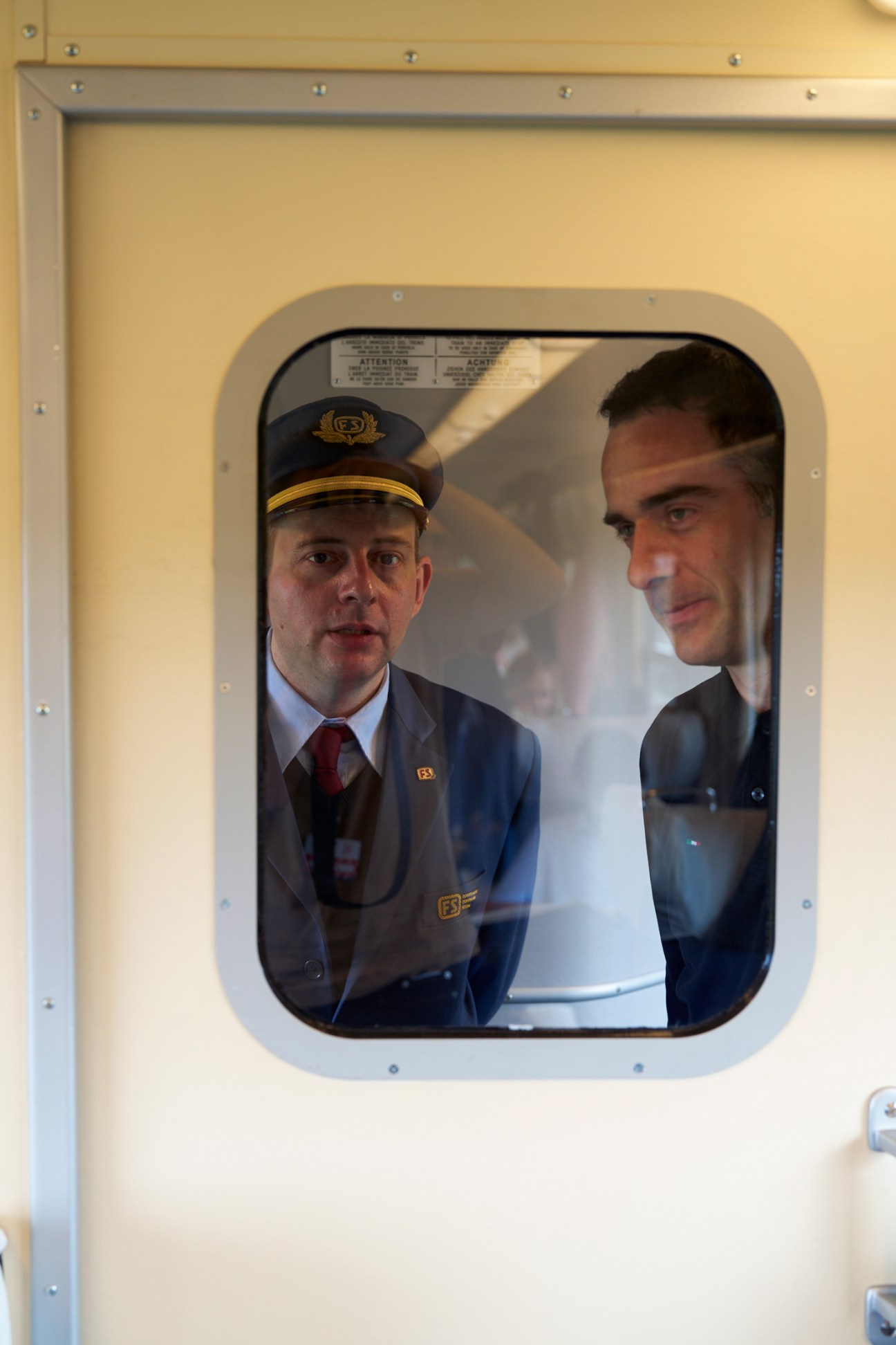 Train conductor in uniform cap speaking with passenger through window of vintage Italian railway car