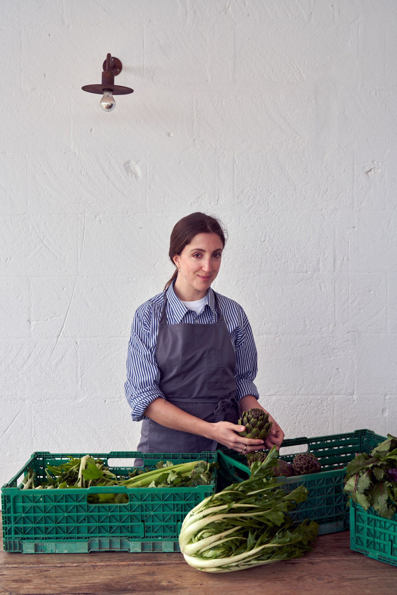 Chef Giorgia Eugenia Goggi in striped shirt and apron handling fresh vegetables with green crates nearby