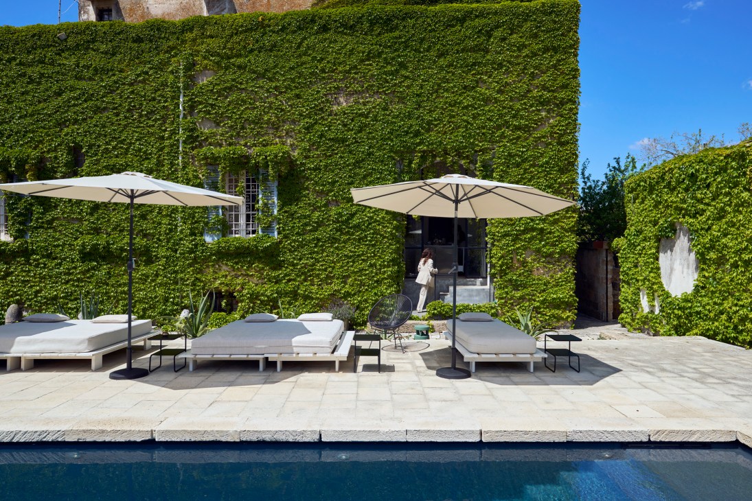 White outdoor loungers with beige umbrellas beside a swimming pool at a luxury hotel with ivy-covered building
