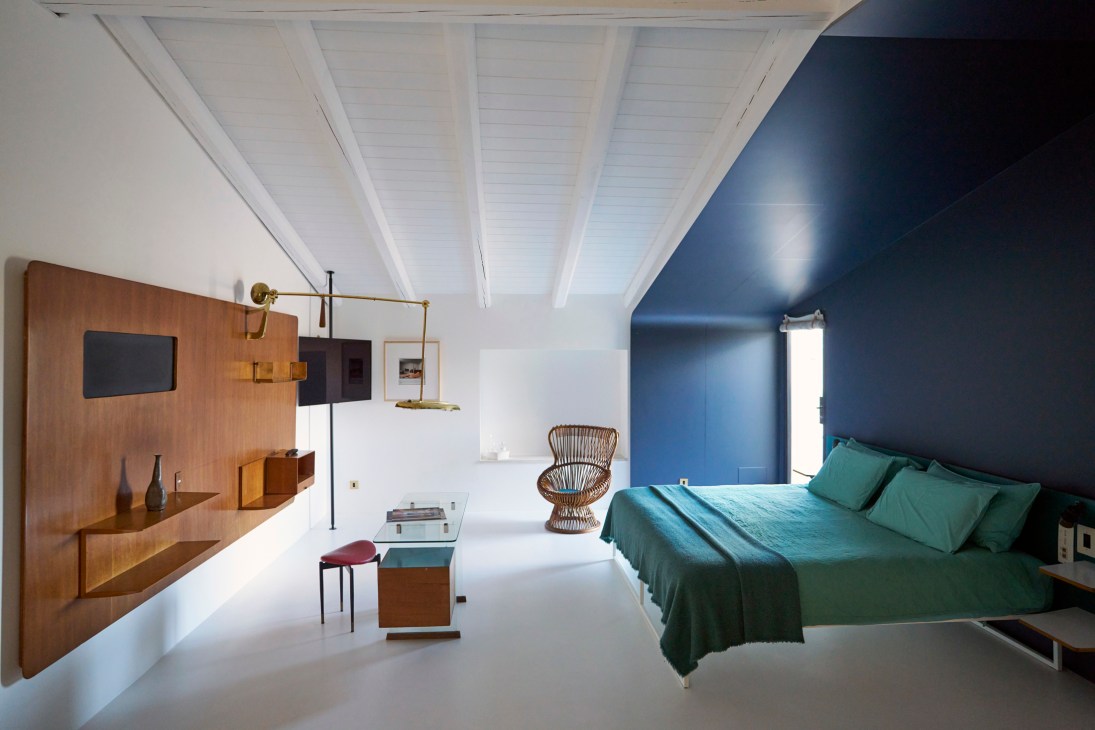 Modern hotel bedroom with mid-century furniture, white ceiling beams, blue accent wall and green bedding