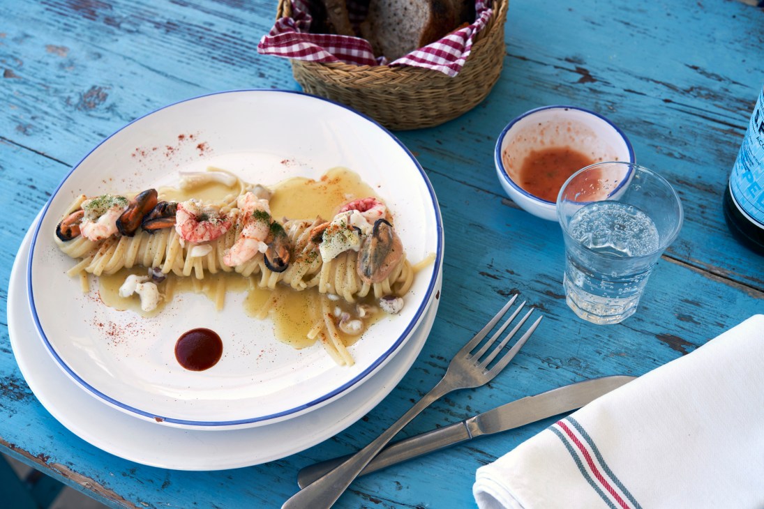 Artfully plated seafood pasta dish with mussels, shrimp and herbs on white plate with sauce drizzles