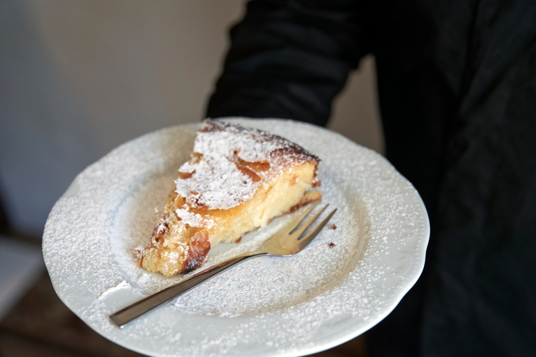 Slice of cake dusted with powdered sugar on white plate with fork at Trattoria Le Zie