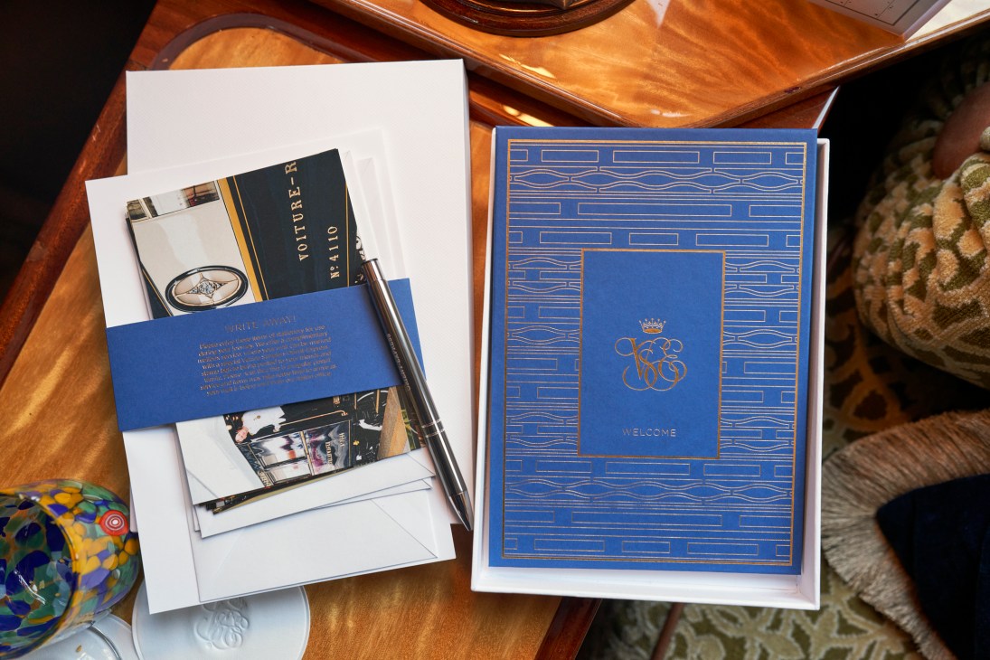 Blue leather-bound welcome folder with crown monogram and complimentary stationery on wooden train table