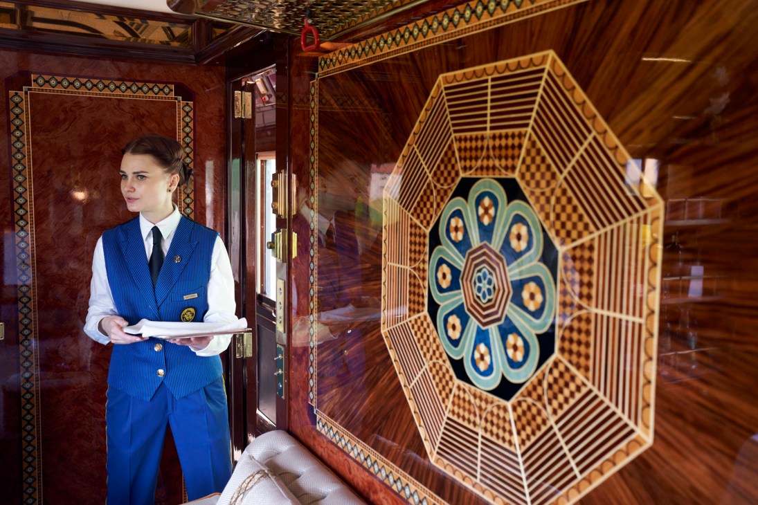 Train attendant in blue uniform standing in ornate wooden carriage with decorative ceiling medallion