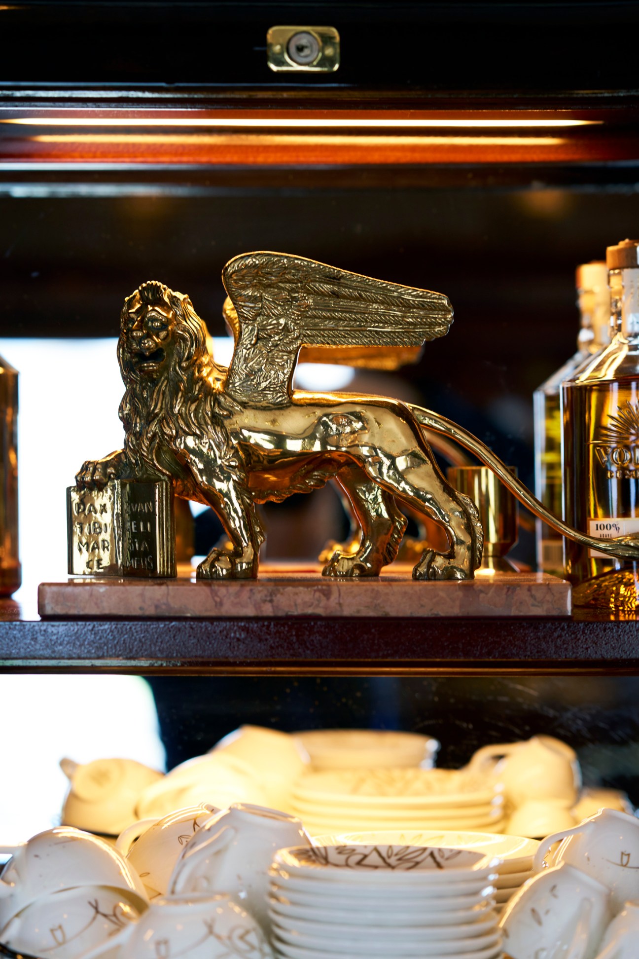 Golden winged lion statue displayed on train shelf with decorative glassware and bottles