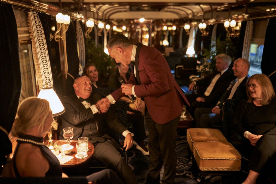 Singer-trombonist Luigi de Gaspari greets passengers in the luxurious Orient Express bar car with ornate lighting