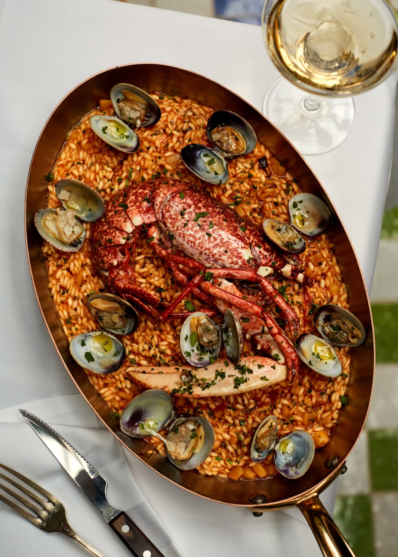 Lobster and seafood risotto with clams in a copper pan alongside white wine