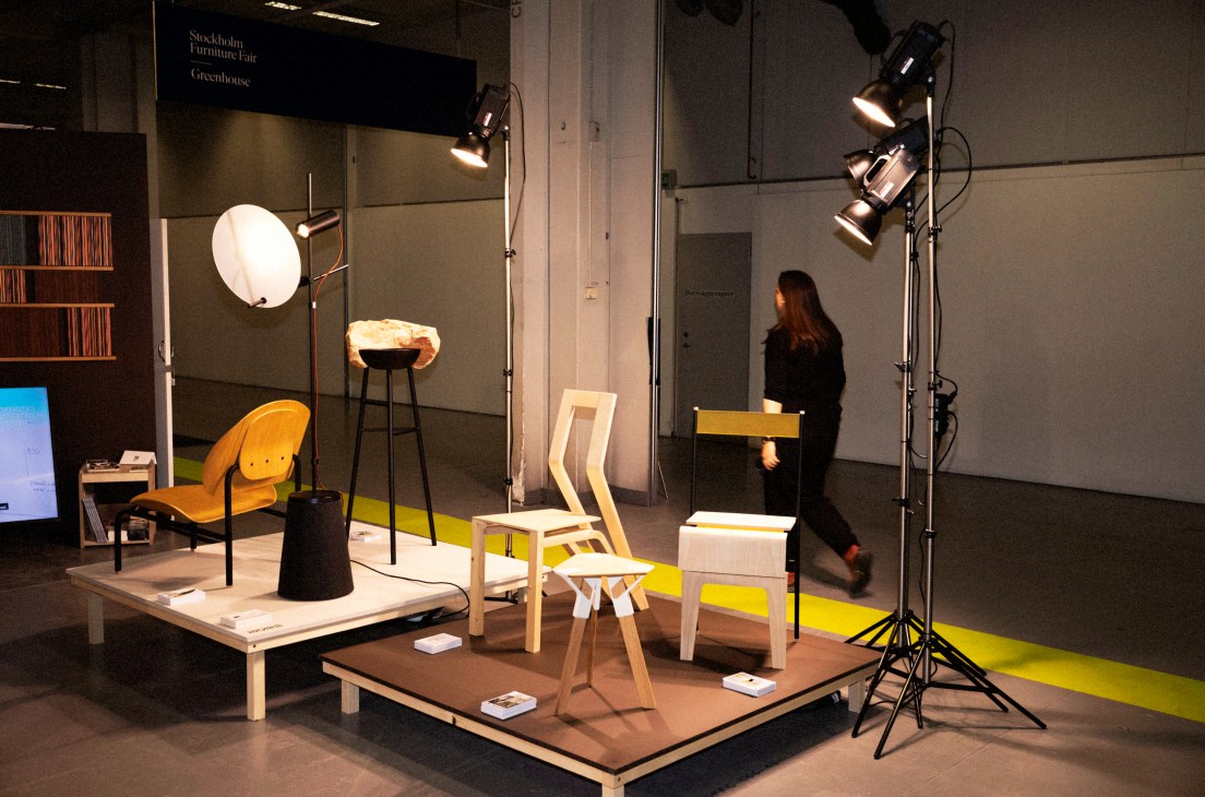 Modern furniture display with professional photography lighting equipment and person walking in background at trade fair