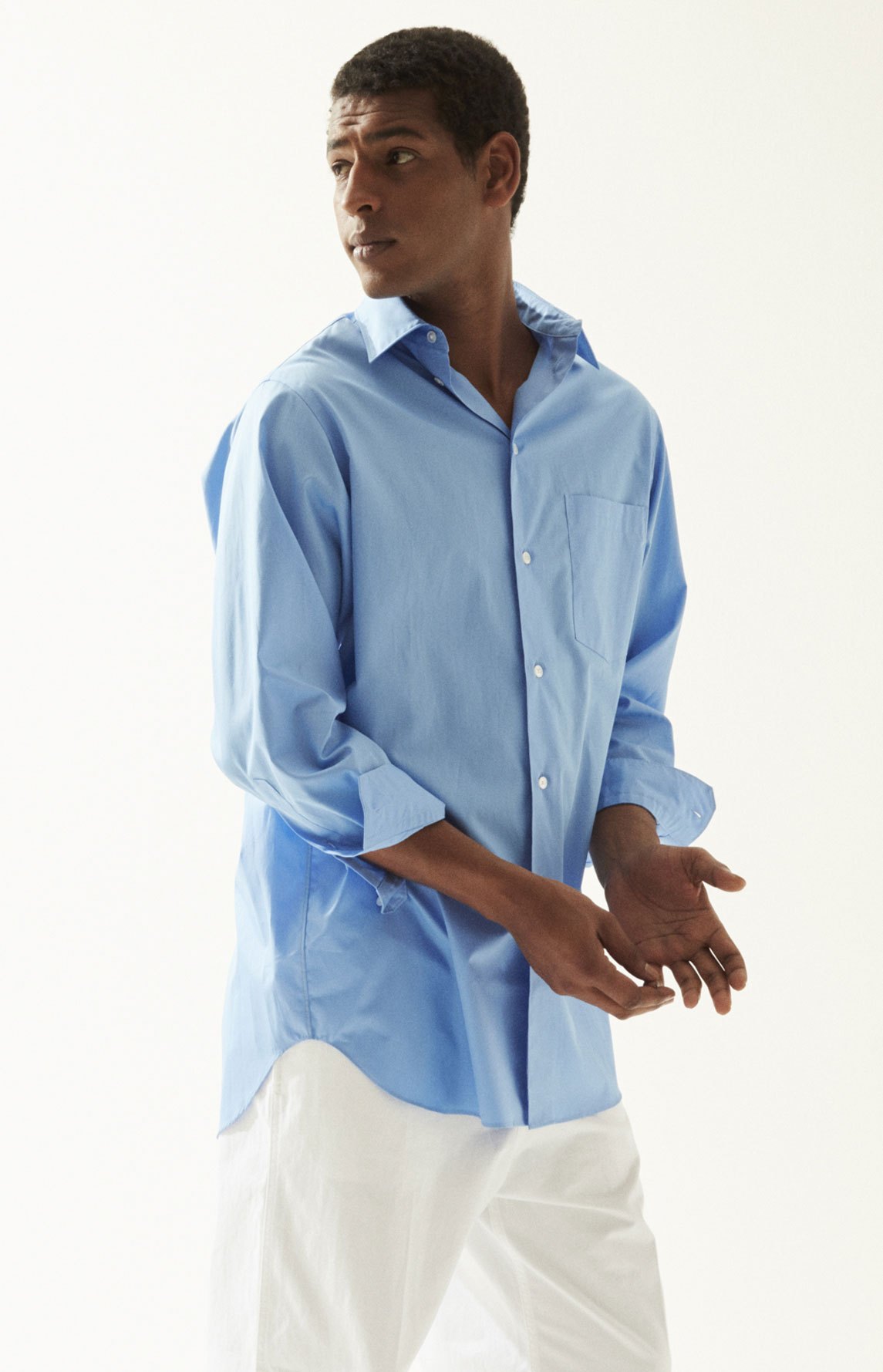 Man wearing a light blue button-up shirt and white trousers by Loeff.