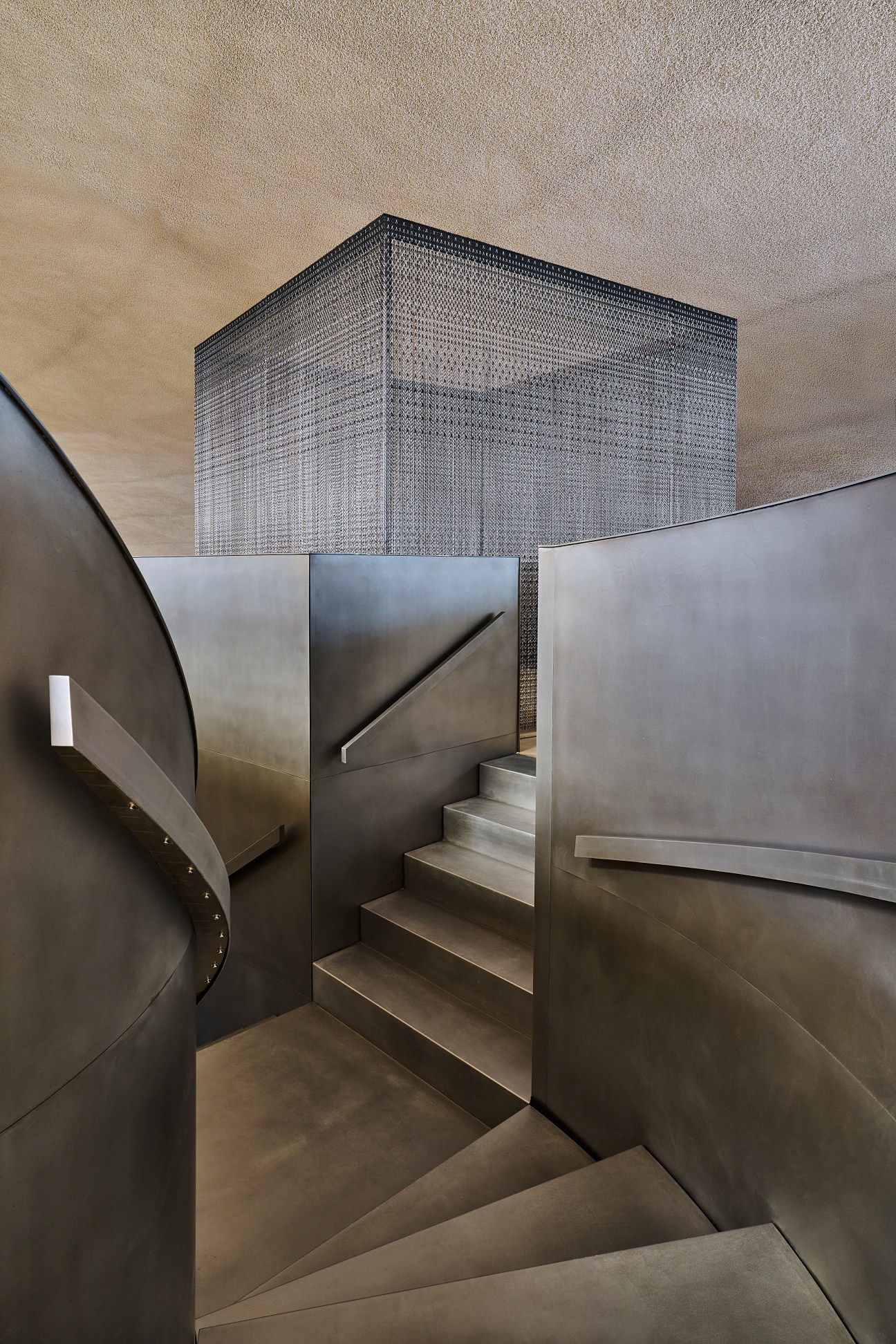 Modern staircase with metal walls and steps leading upward toward a geometric patterned structure.