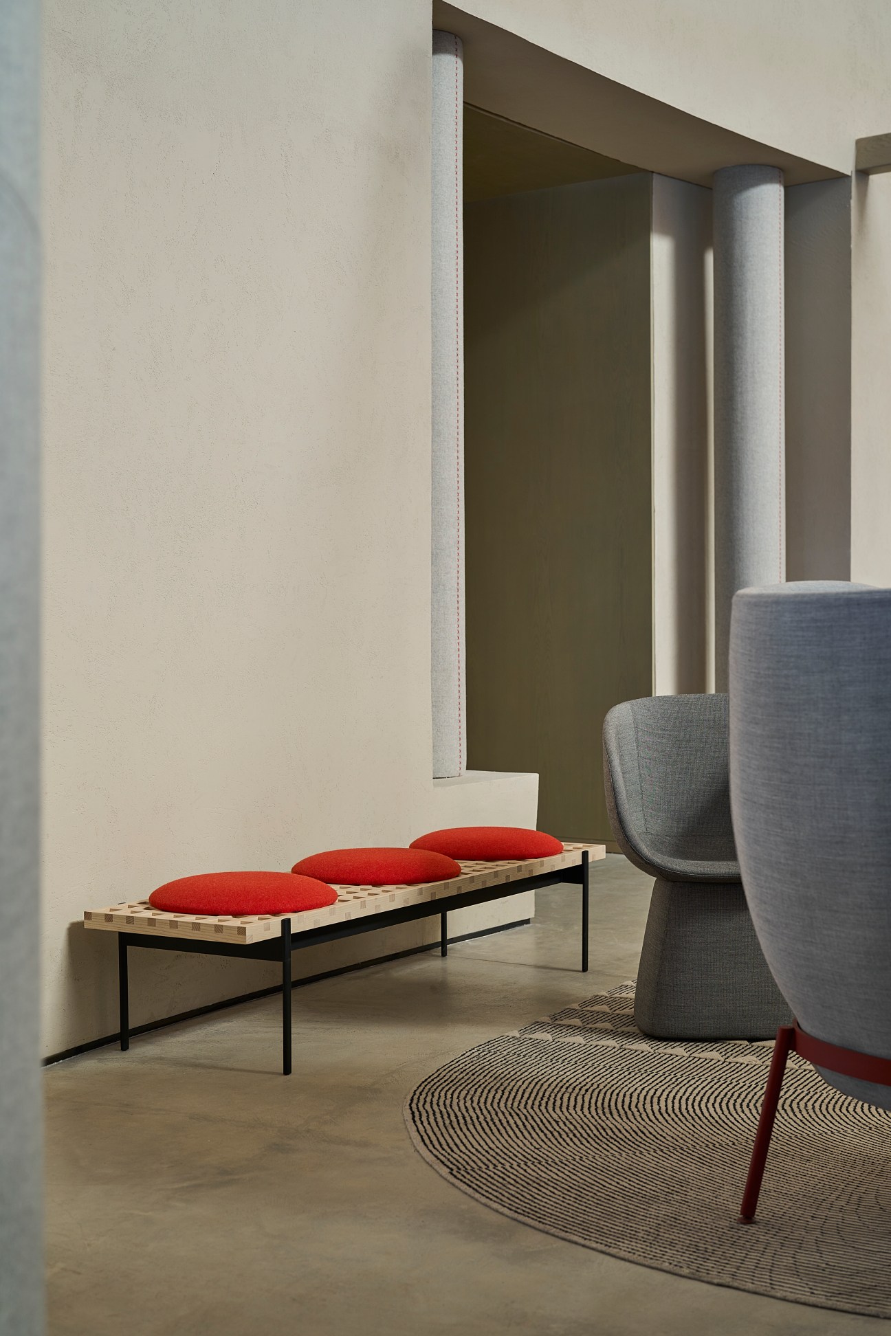 Interior space featuring a bench with red cushions, gray upholstered chairs, and minimalist architectural design by Agata Kurzela.
