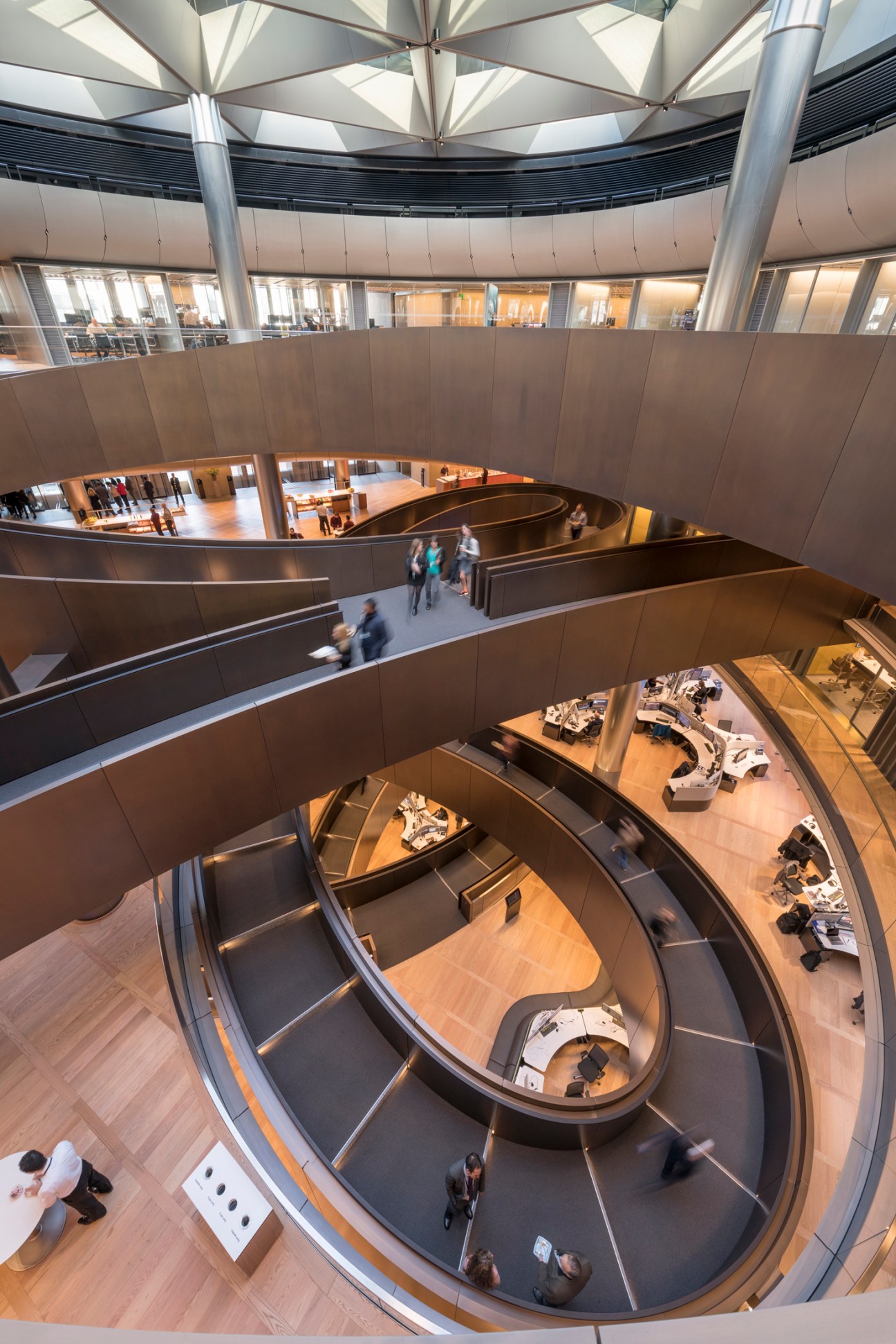Modern spiral ramp with curved balconies and people walking through multi-level atrium space