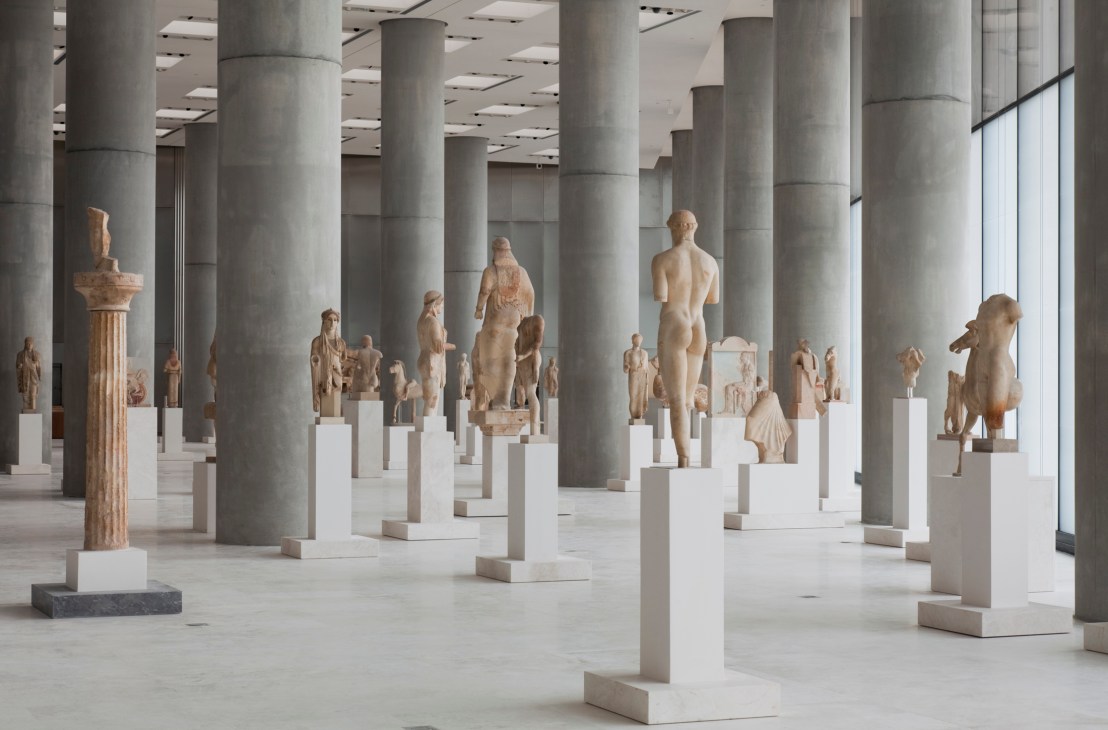 Interior view of Acropolis Museum showing ancient marble statues displayed on white pedestals among concrete columns