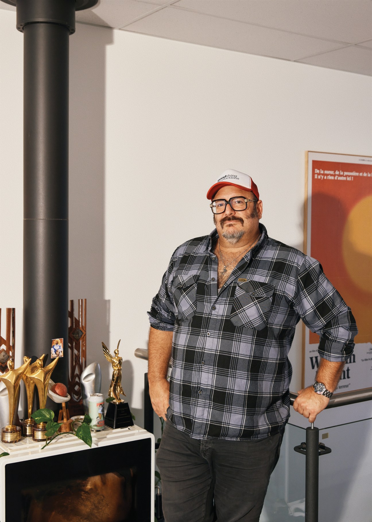Nick Batzias, founder of Goodthing Productions, stands in an office wearing a plaid shirt and red cap.