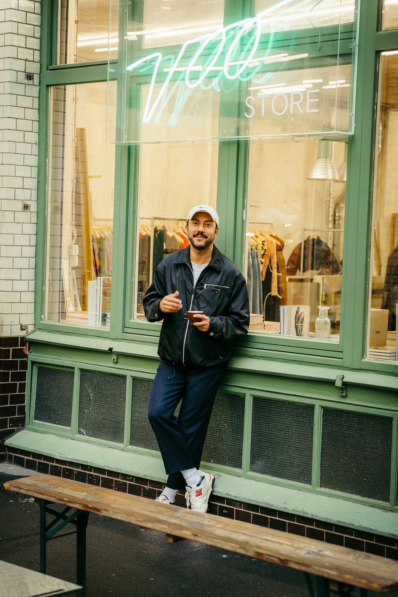 Voo Store owner Yasin Müjdeci standing in front of the green-framed storefront with neon signage.