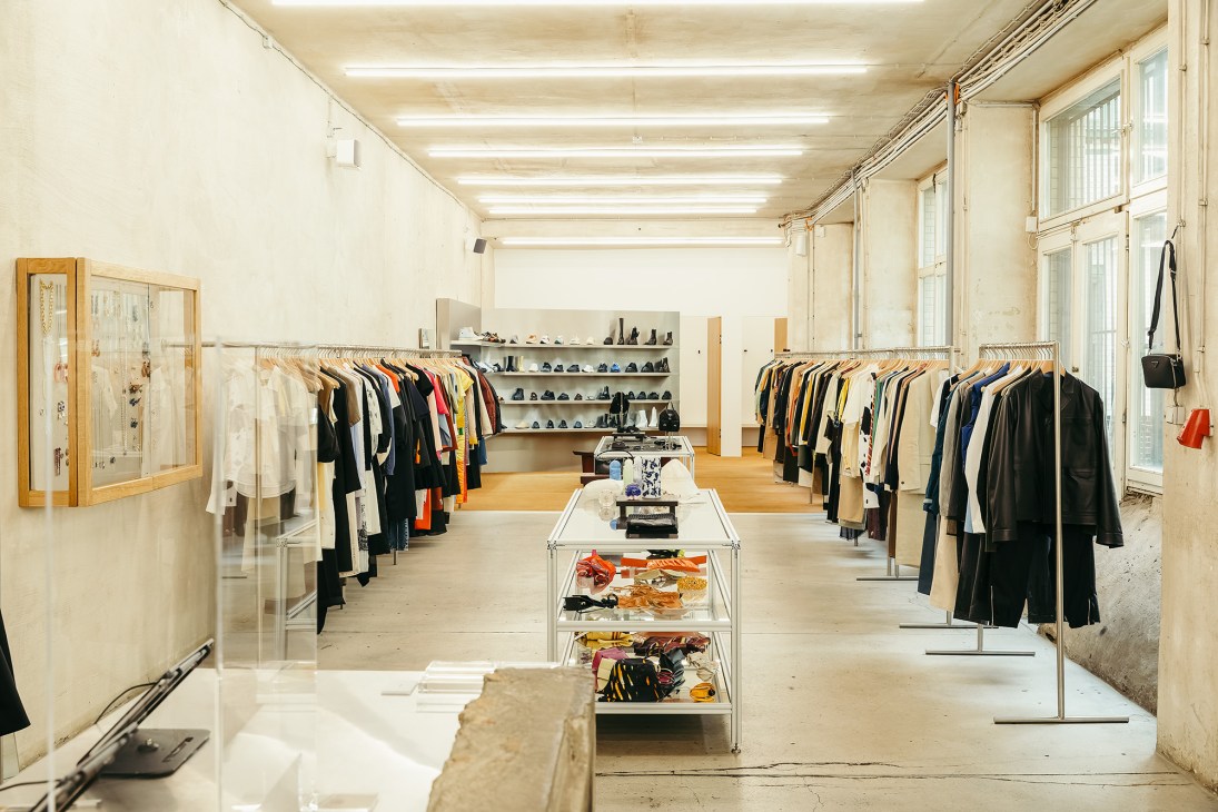 Interior of Voo Store showing clothing racks, shelves of shoes, and a central display table in a concrete space.