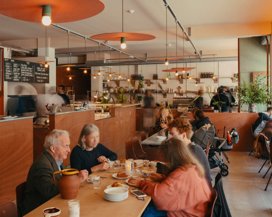 Interior of Big Jo bakery showing diners at communal tables with orange pendant lights and open kitchen