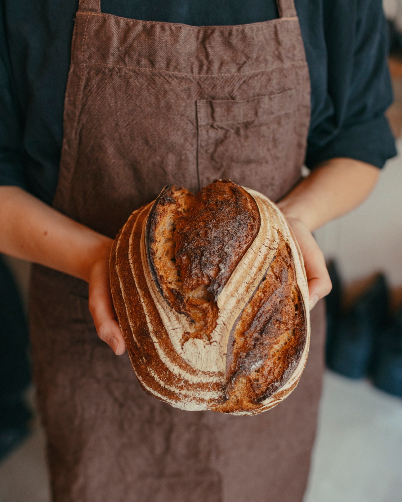 Hands holding a freshly baked sourdough loaf with decorative scoring patterns at Big Jo bakery