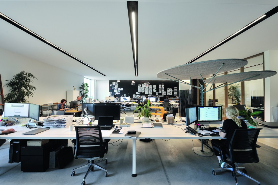 Modern open-plan office with white desks, black chairs, computer monitors and plants in a bright contemporary workspace