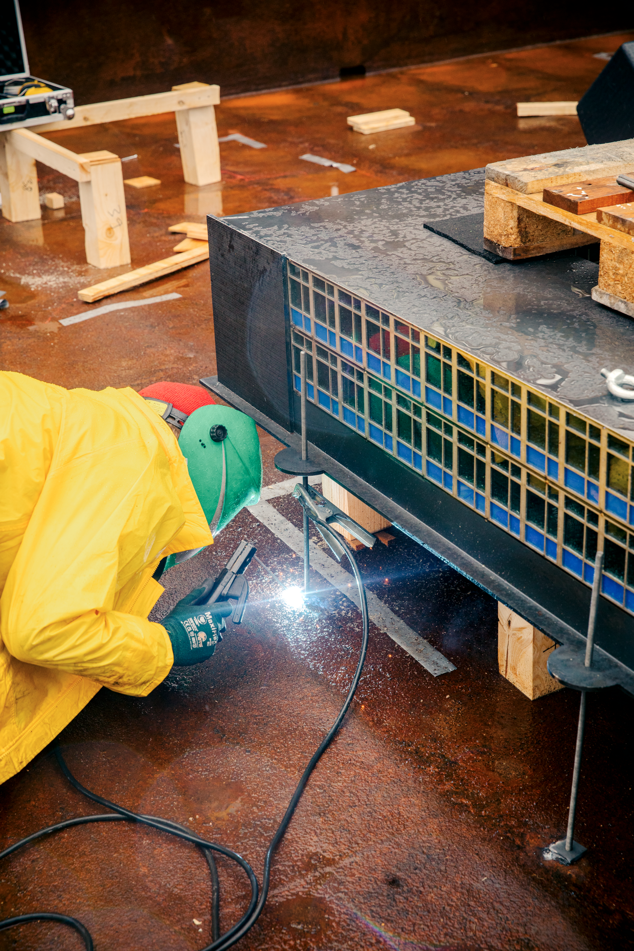 A person in a yellow raincoat welding with protective gear while working on a sculpture or art installation