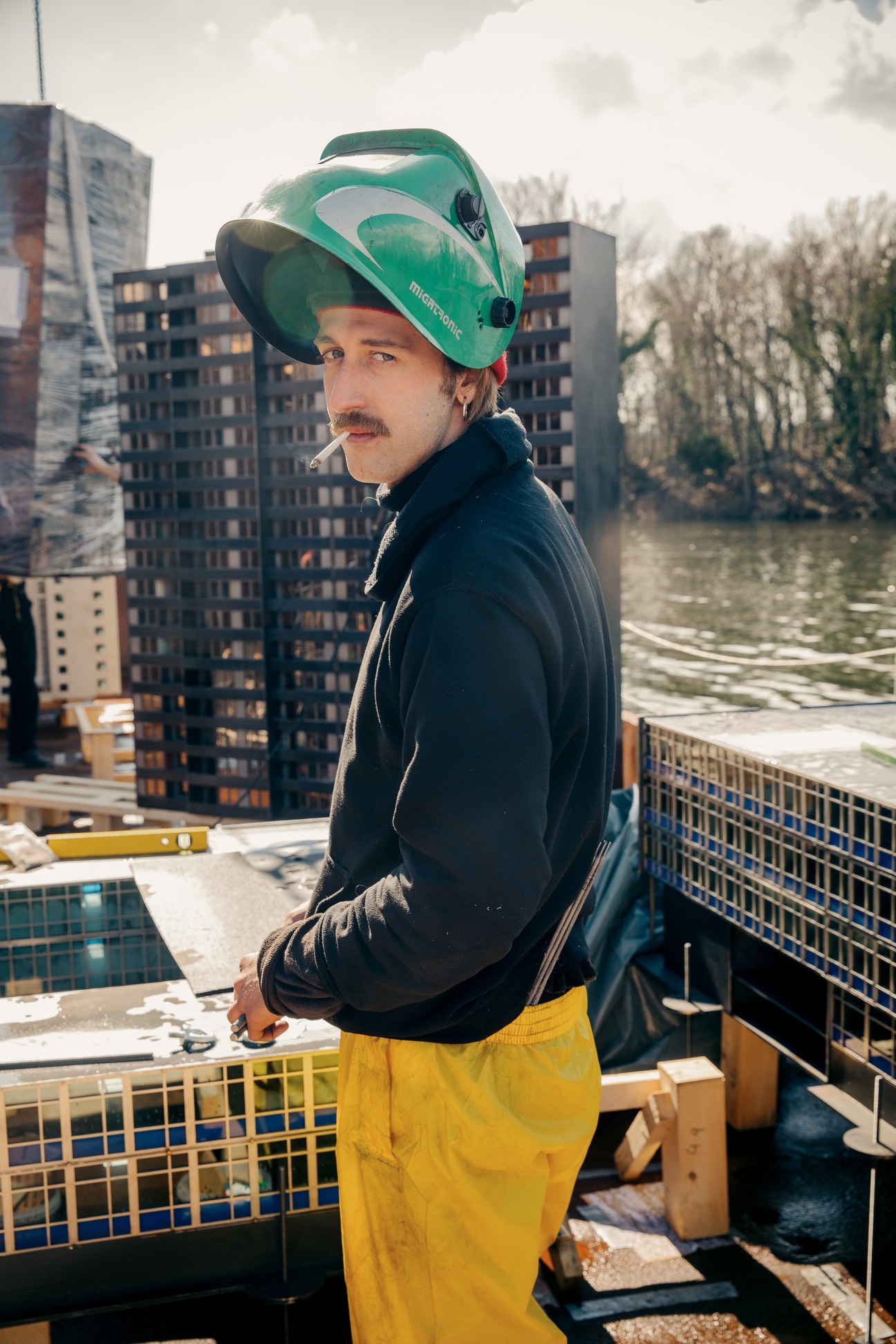 Construction worker in green welding helmet taking a cigarette break on a barge