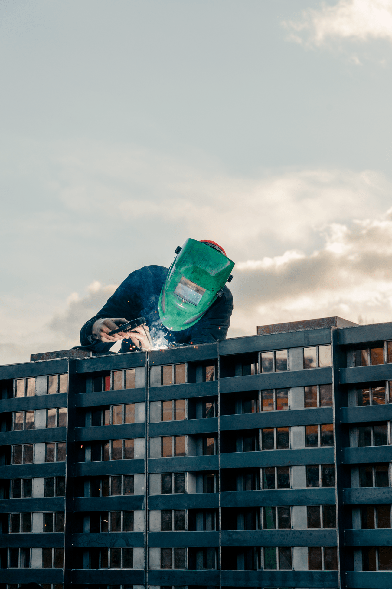 Worker in green welding helmet and dark clothing welding on an industrial barge