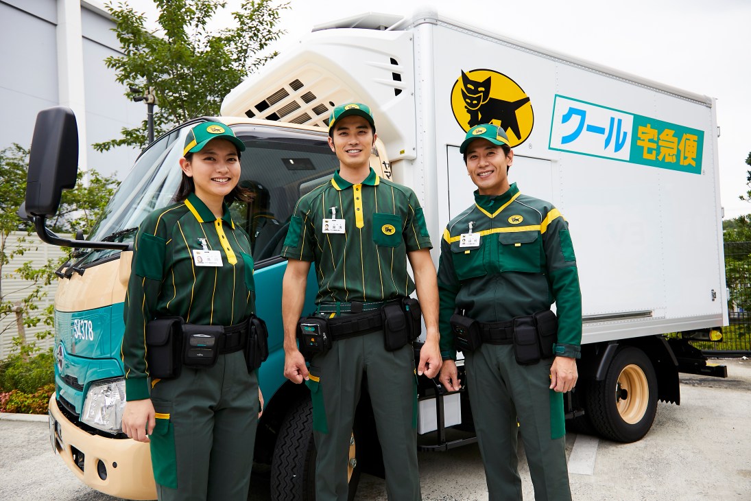 Three Yamato delivery employees in new uniforms standing in front of delivery truck with black cat logo