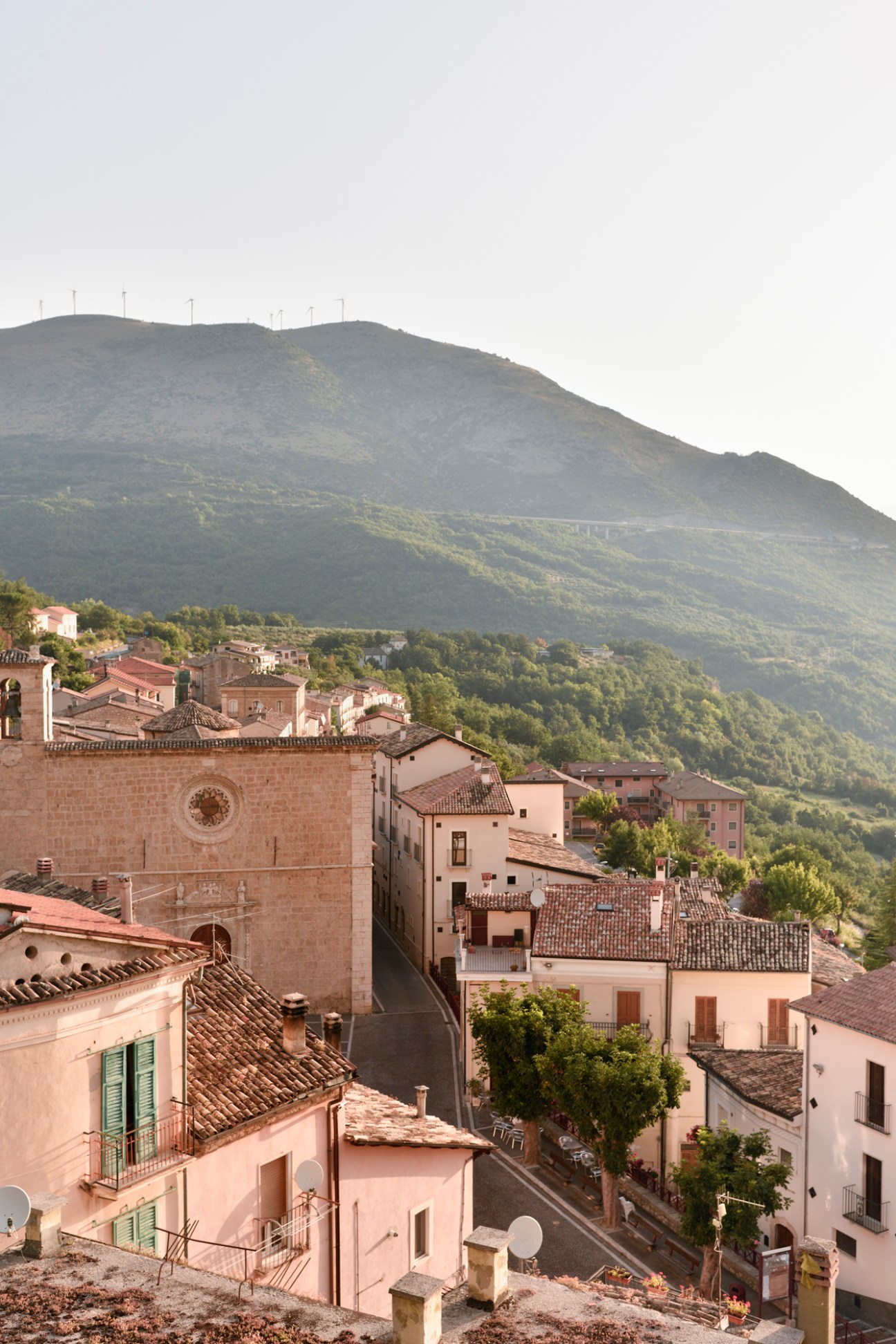 Medieval village of Anversa degli Abruzzi with terracotta-roofed buildings nestled in a forested valley beneath dramatic mountain peaks.