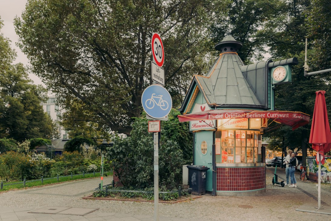 Traditional Berlin currywurst kiosk with distinctive architecture, red signage, and customers gathered outside