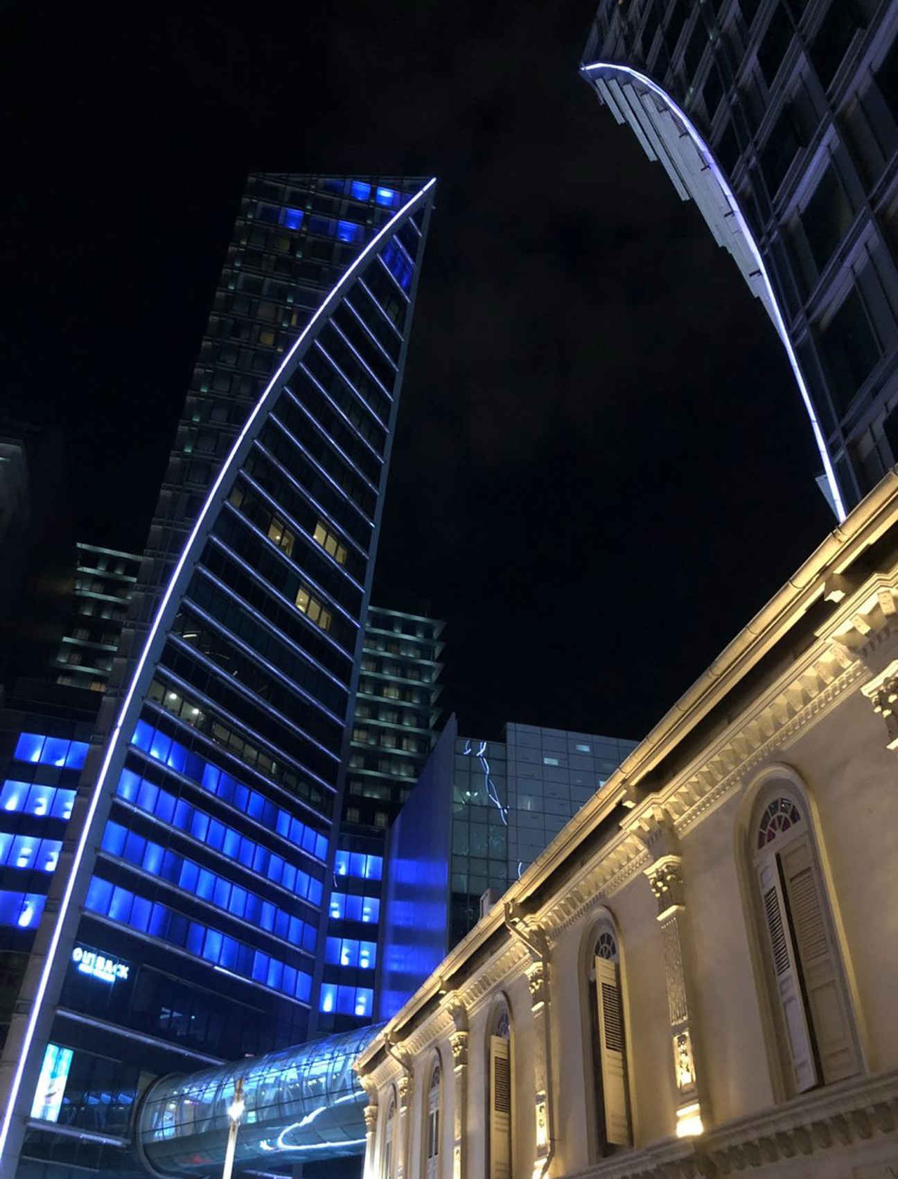 Night view of modern illuminated buildings with blue lighting contrasting historic colonial architecture below