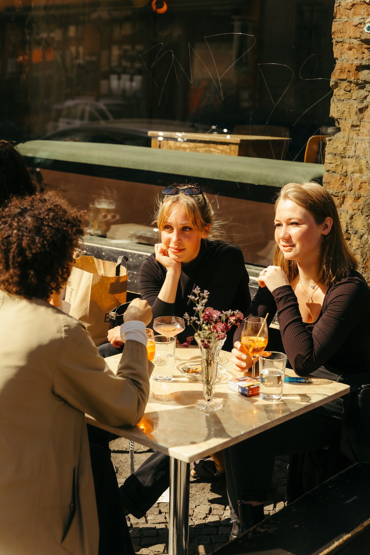 Three women enjoy drinks and conversation at an outdoor table in front of Café Luzia in Berlin's Kreuzberg district.
