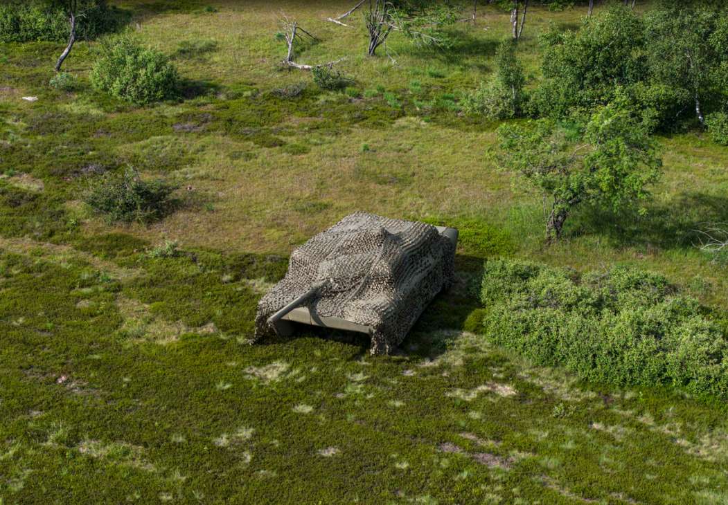 Aerial view of an inflatable military tank decoy camouflaged on green terrain.