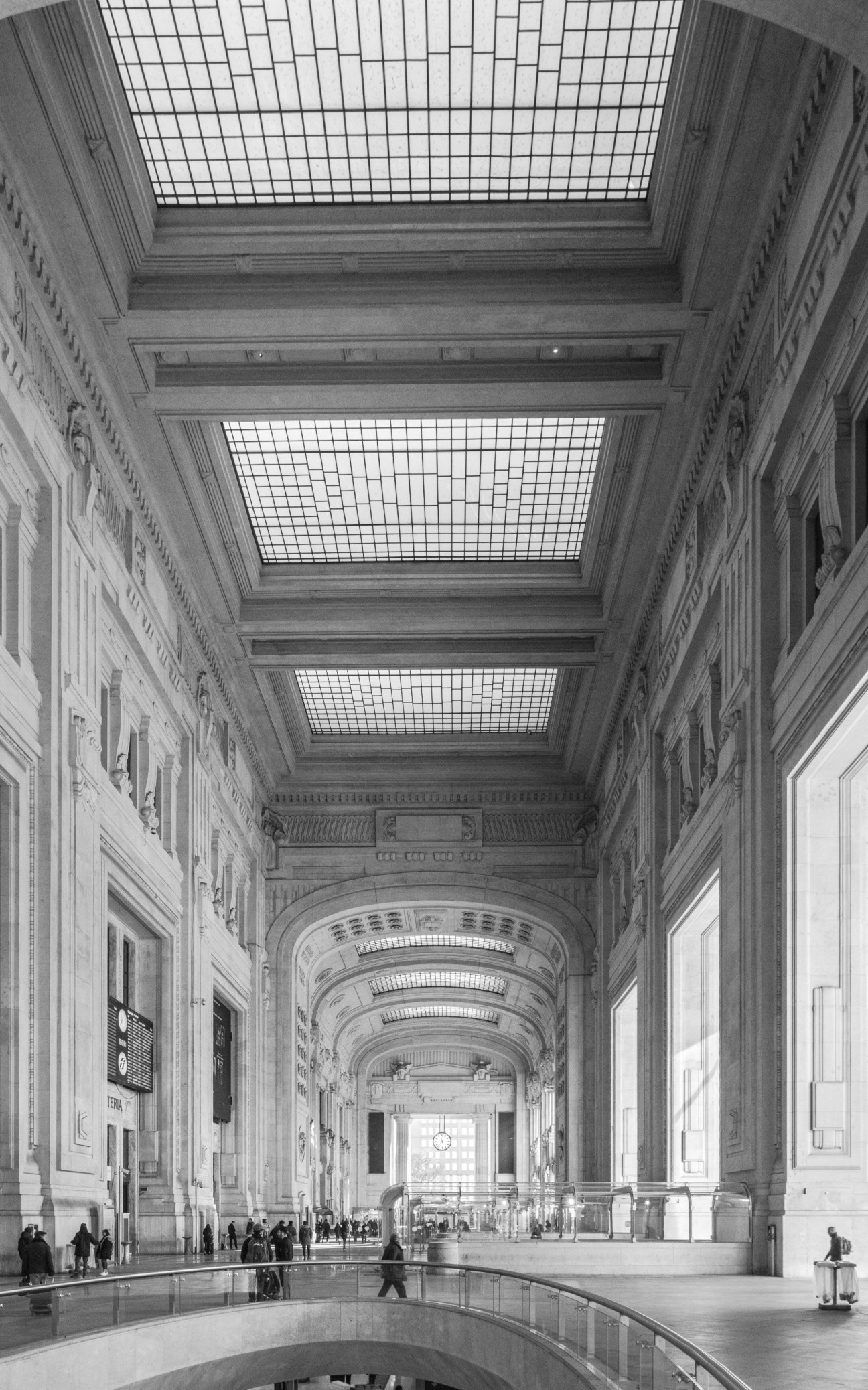 Black and white photograph of Milan Centrale railway station interior with high vaulted ceilings and classical architecture