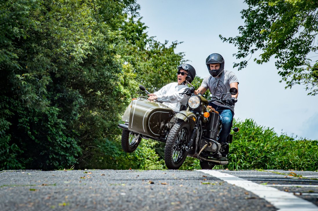Ural motorcycle with sidecar airborne on winding road with driver and passenger in helmets