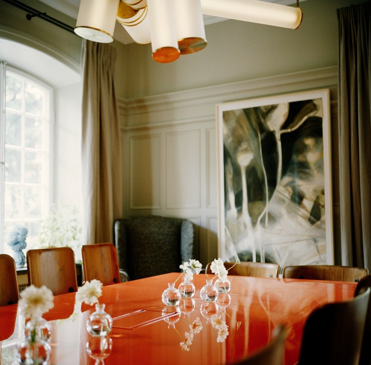 Glossy red lacquered dining table with white cylindrical pendant lights overhead and white flowers in glass vases.