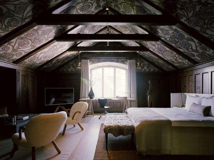 Cozy attic bedroom with exposed wooden beams, decorative painted ceiling, modern furniture and arched window