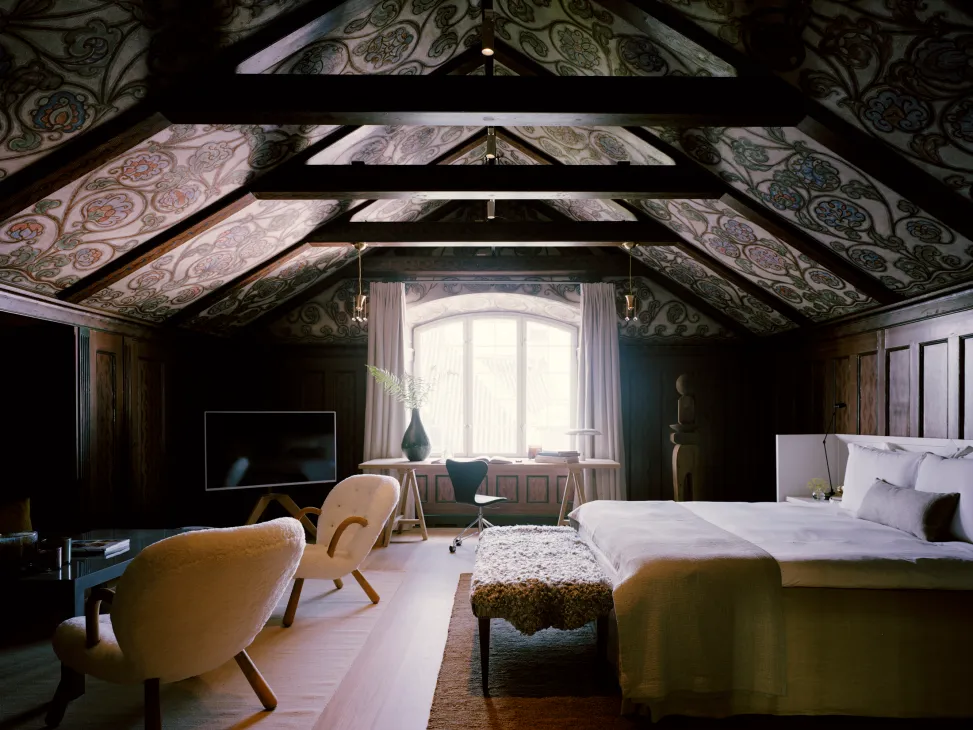 Cozy attic bedroom with exposed wooden beams, decorative painted ceiling, modern furniture and arched window