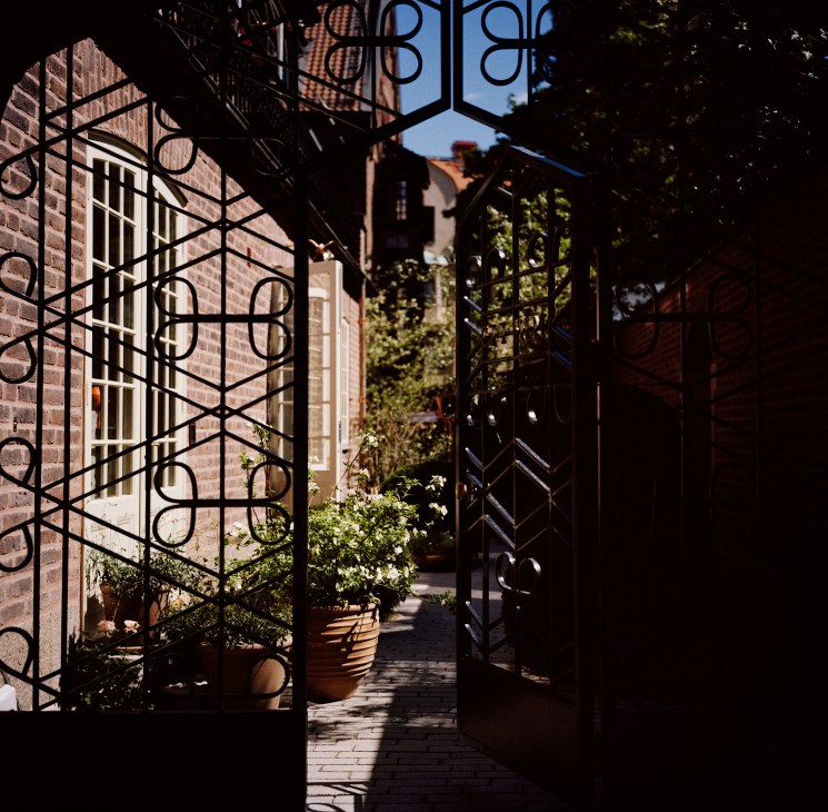 Ornate wrought-iron gates with Ett Hem branding forged into the metalwork, flanking a brick building entrance.