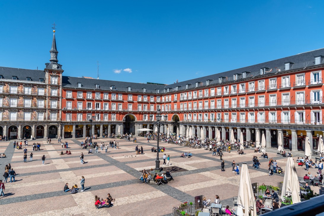 Plaza Mayor in Madrid with red historic buildings, outdoor dining, and people socializing in the central square