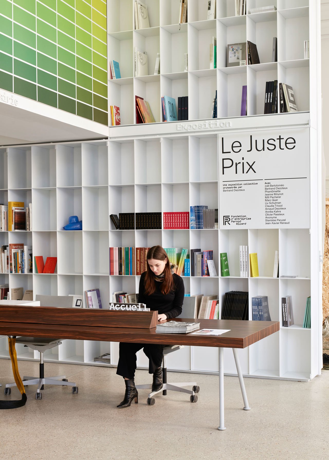 Woman reading at wooden desk in modern library with white modular bookshelves and colorful wall display