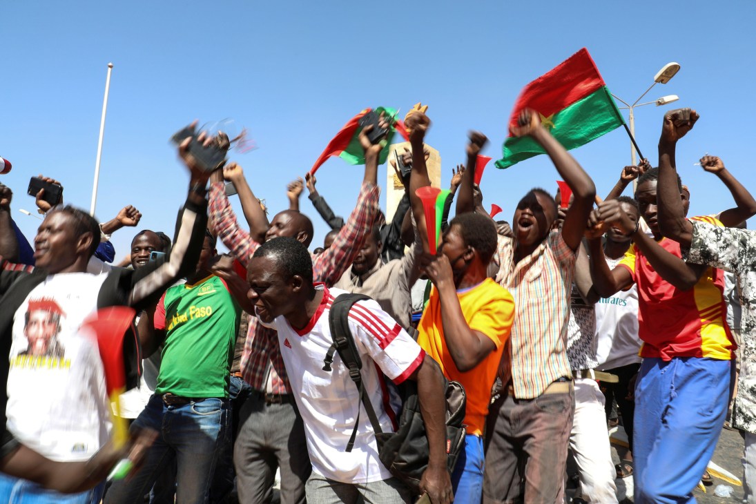 A crowd of protesters with raised fists holding flags with red and green colors during a demonstration