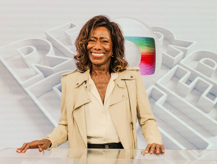 Glória Maria sitting at a broadcast desk in a television studio