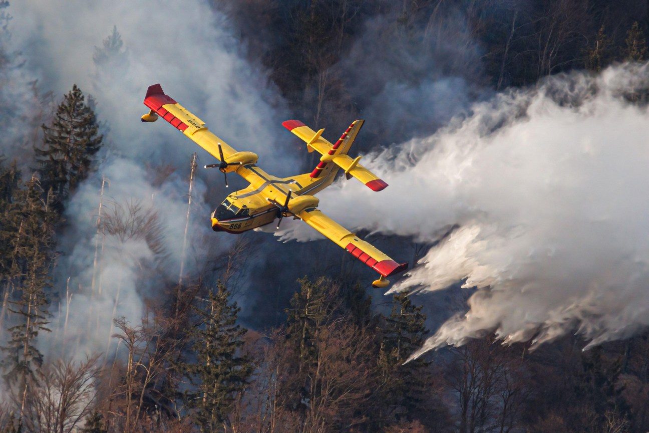 Red and yellow Canadair water-bombing aircraft flying over forested landscape